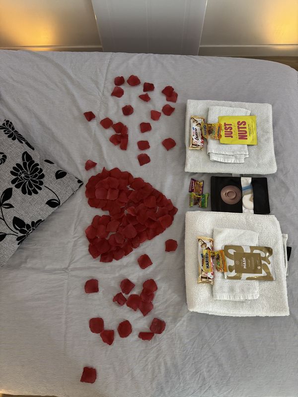 Lit décoré d'un cœur en pétales de rose, serviettes et douceurs